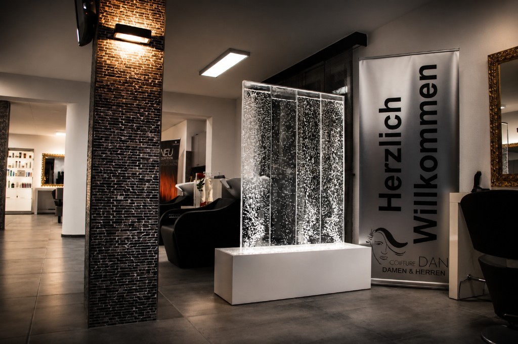 Salon-Innenraum mit beleuchteter Wasserwand und Willkommensbanner